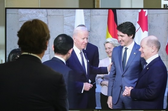 2022年3月24日，在比利時布魯塞爾的北約總部，一名男子觀看屏幕上美國總統(tǒng)拜登（右四）、歐盟委員會主席馮德萊恩（右三）、加拿大總理特魯多（右二）、德國總理朔爾茨（右一）出席七國集團(tuán)峰會合影儀式的畫面。新華社記者鄭煥松攝