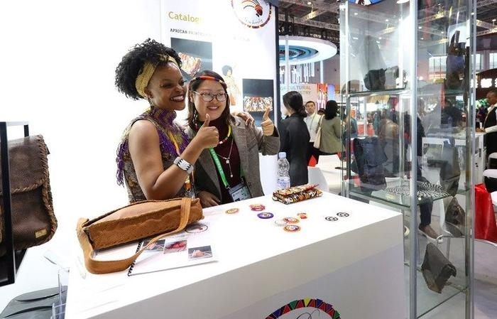 11月6日，一位參觀者（右）在第六屆進(jìn)博會國家展南非展臺試戴傳統(tǒng)首飾。