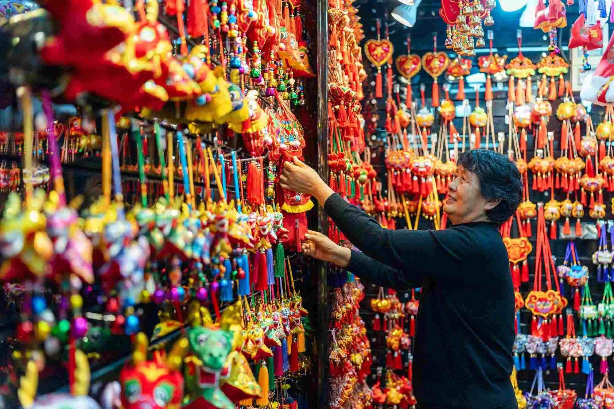 2023年12月11日，金華義烏國際商貿(mào)城，龍年喜慶用品掛滿攤位，顧客正在挑選中。