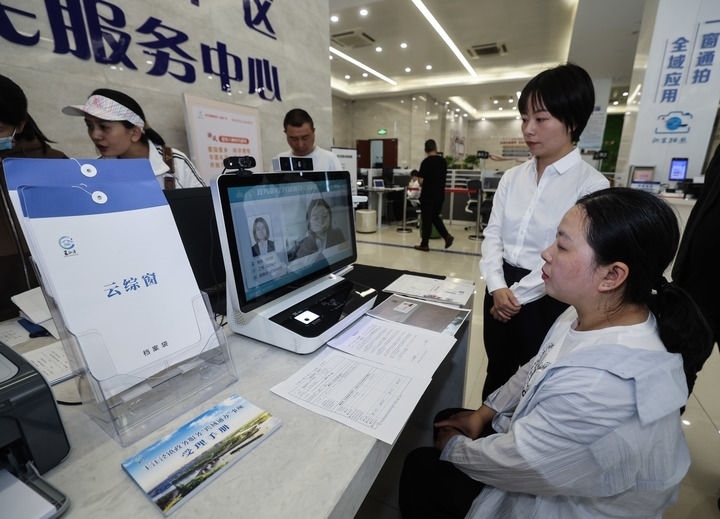 在浙江省嘉興市秀洲區(qū)王江涇鎮(zhèn)便民服務(wù)中心的“跨域通辦·云綜窗”窗口，辦理開業(yè)登記的個體工商戶（右一）通過該系統(tǒng)與江蘇省蘇州市吳江區(qū)盛澤鎮(zhèn)行政審批局工作人員視頻連線，進行身份讀取及材料線上審核（2024年5月9日攝）。新華社記者 徐昱 攝