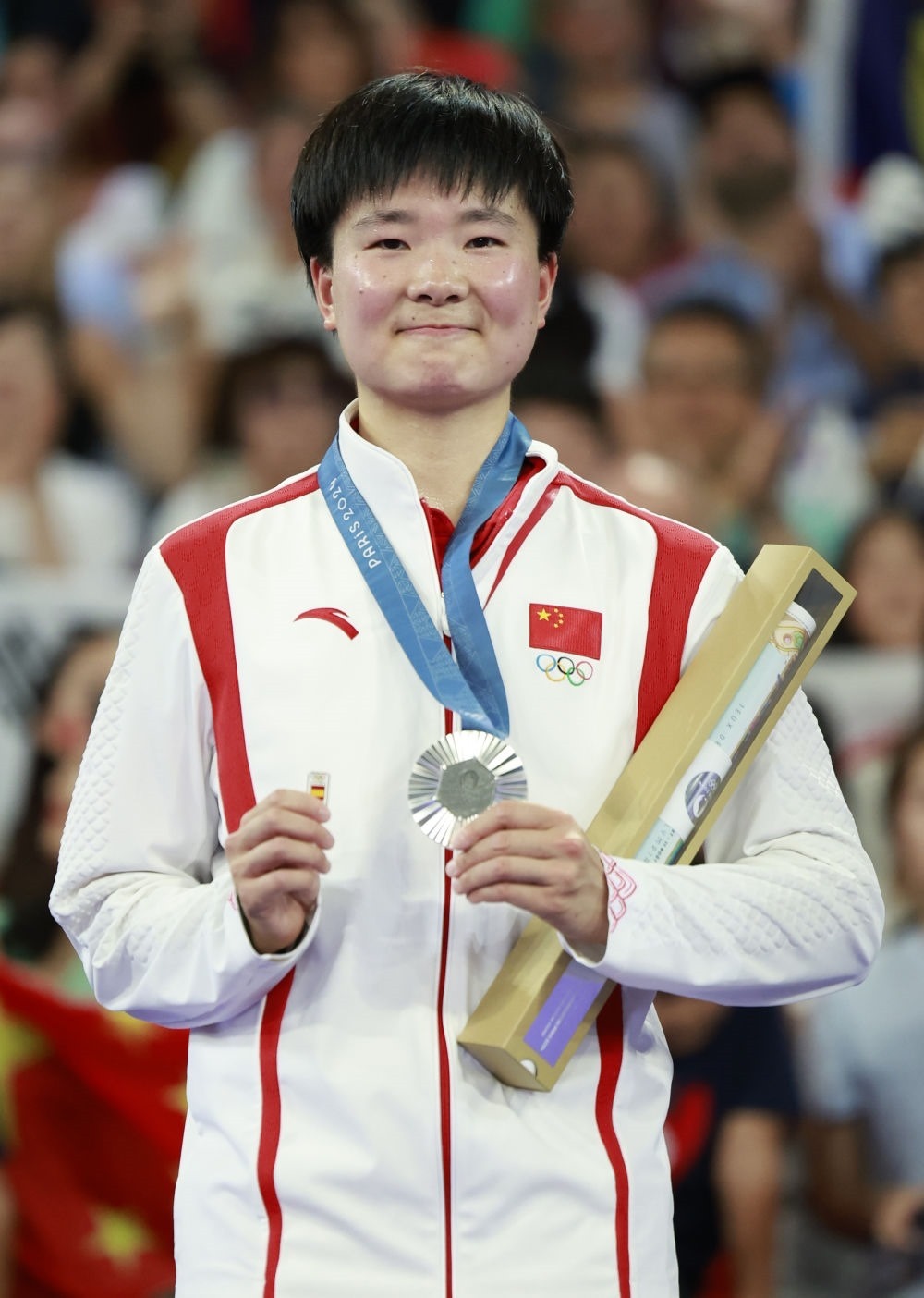 巴黎奧運(yùn)會(huì)羽毛球女子單打亞軍、中國選手何冰嬌在頒獎(jiǎng)儀式上一手握著銀牌，一手握著西班牙奧委會(huì)徽章（2024年8月5日攝）。新華社記者 任正來 攝