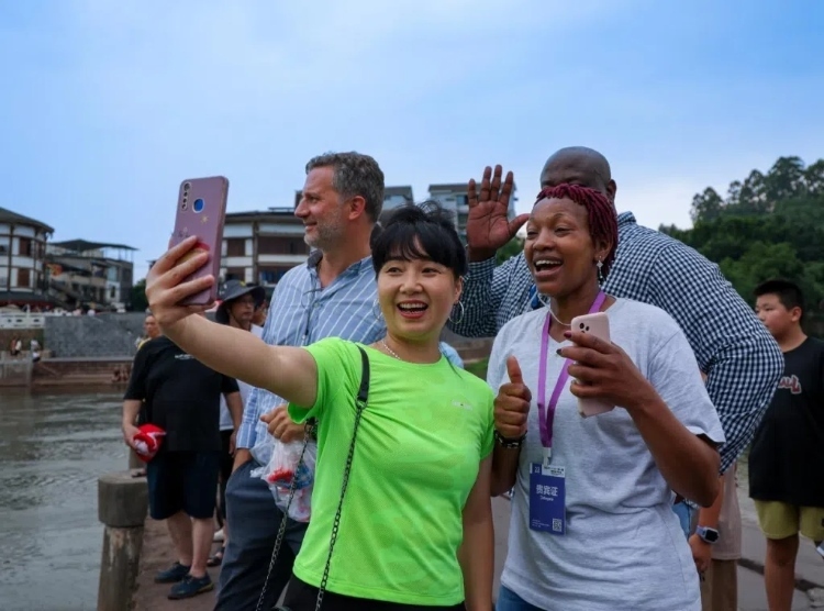 2024“一帶一路”媒體合作論壇聯(lián)合采訪調(diào)研行成員在樂山蘇稽古鎮(zhèn)與游客合影留念。本報(bào)記者 伊霄攝