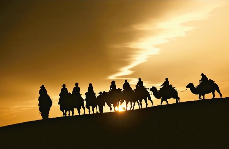 新時(shí)代以來(lái)，文化和旅游深度融合發(fā)展體制機(jī)制不斷健全，成功走出了一條獨(dú)具特色的中國(guó)旅游發(fā)展之路。圖為2024年9月1日清晨，游客在甘肅省敦煌市鳴沙山月牙泉景區(qū)乘騎駱駝，欣賞大漠風(fēng)光，體驗(yàn)絲路風(fēng)情。 新華社發(fā) 張曉亮/攝