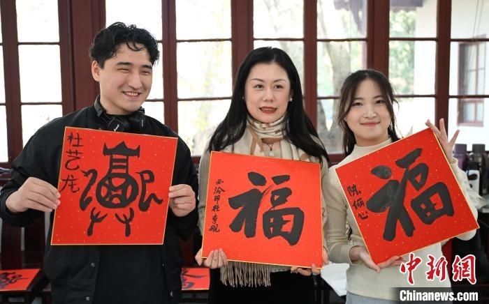 1月20日，外籍留學(xué)生和西泠印社社員李硯(中)展示各自創(chuàng)作的福貼。當(dāng)日，來(lái)自巴西、馬來(lái)西亞、加納、哈薩克斯坦的外籍留學(xué)生在浙江杭州西泠印社體驗(yàn)福貼、春聯(lián)和篆刻，感受古老的中國(guó)傳統(tǒng)文化。中新社記者 王剛 攝